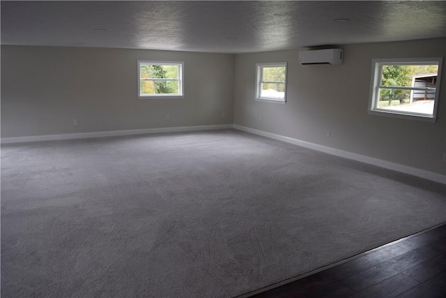 empty room featuring a wall unit AC, plenty of natural light, a textured ceiling, and hardwood / wood-style flooring