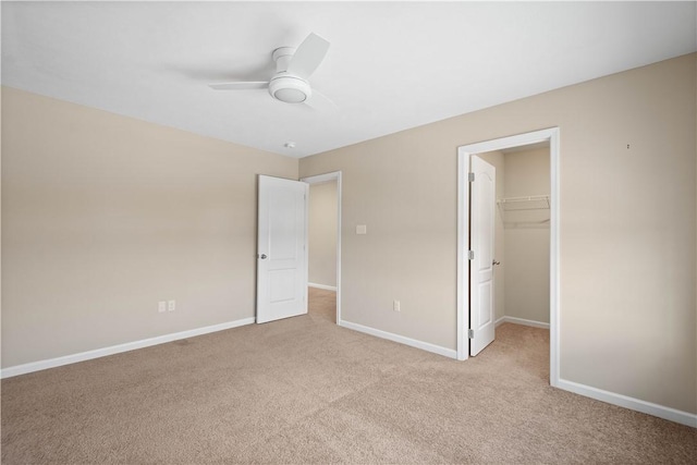 unfurnished bedroom featuring a walk in closet, a closet, ceiling fan, and light colored carpet