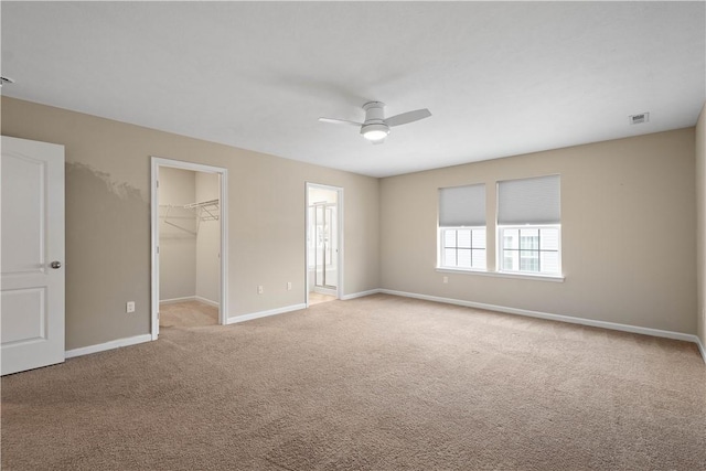 unfurnished bedroom with a spacious closet, a closet, ceiling fan, and light colored carpet