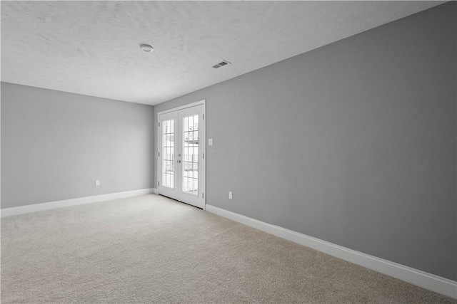 carpeted spare room featuring a textured ceiling and french doors