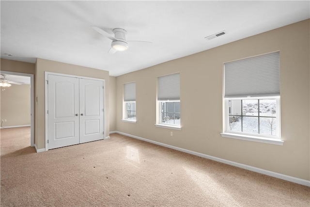 unfurnished bedroom featuring carpet, ceiling fan, a closet, and multiple windows