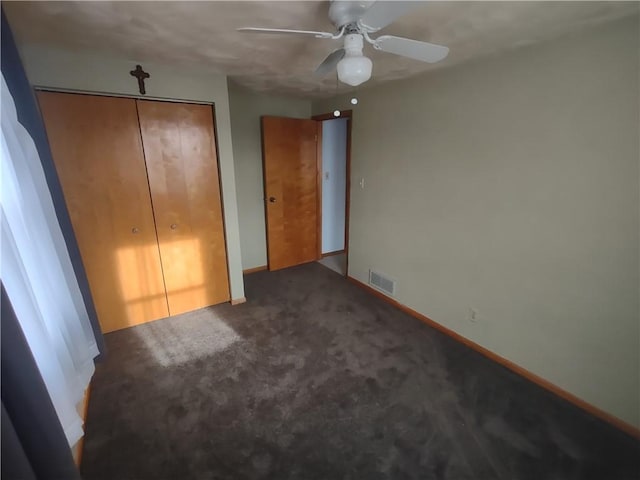 unfurnished bedroom featuring baseboards, visible vents, ceiling fan, dark carpet, and a closet