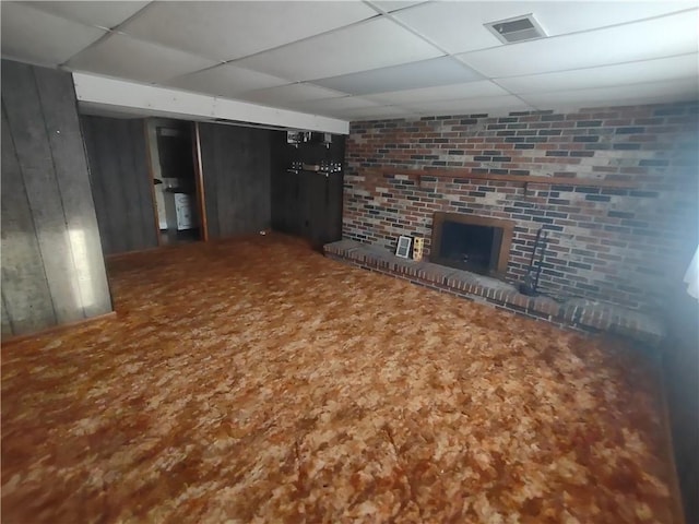 unfurnished living room with a paneled ceiling, a brick fireplace, brick wall, and visible vents