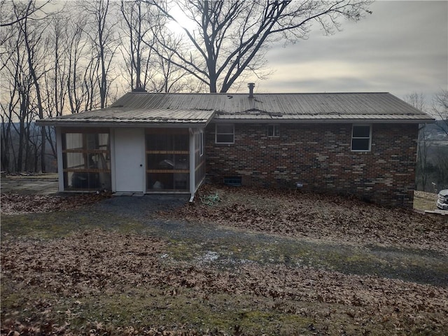 rear view of property featuring metal roof, brick siding, crawl space, and a sunroom