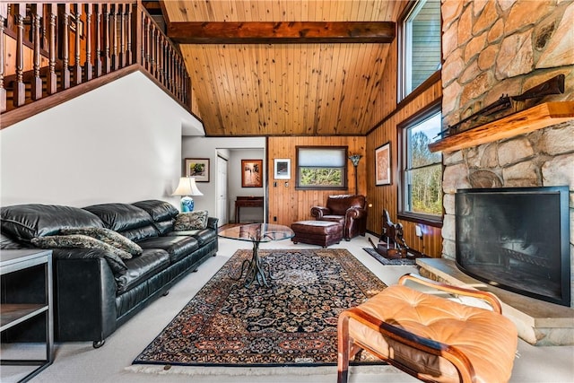 carpeted living room with beam ceiling, wooden ceiling, a stone fireplace, high vaulted ceiling, and wood walls