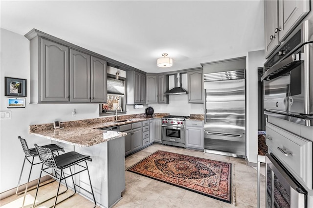 kitchen featuring a kitchen breakfast bar, wall chimney exhaust hood, gray cabinets, premium appliances, and kitchen peninsula