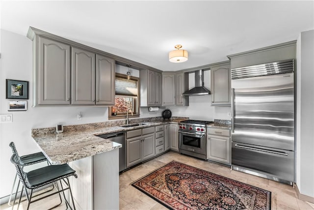 kitchen with kitchen peninsula, a kitchen breakfast bar, premium appliances, sink, and wall chimney range hood