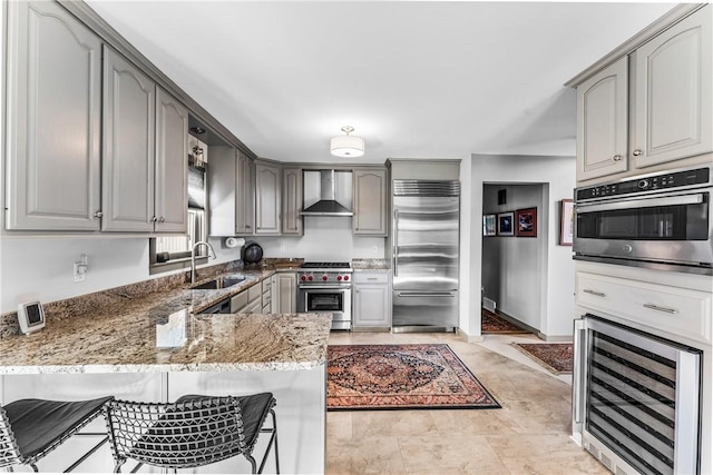 kitchen with sink, wall chimney exhaust hood, premium appliances, wine cooler, and kitchen peninsula