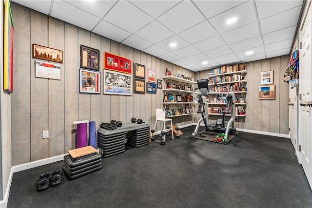 workout area featuring wooden walls and a drop ceiling