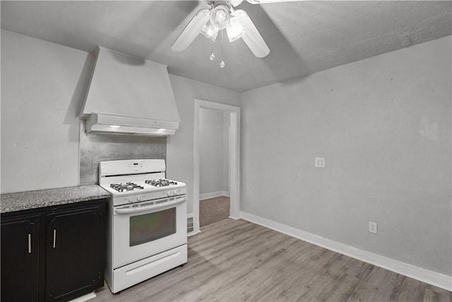 kitchen featuring white range with gas cooktop, ceiling fan, light hardwood / wood-style flooring, and custom exhaust hood