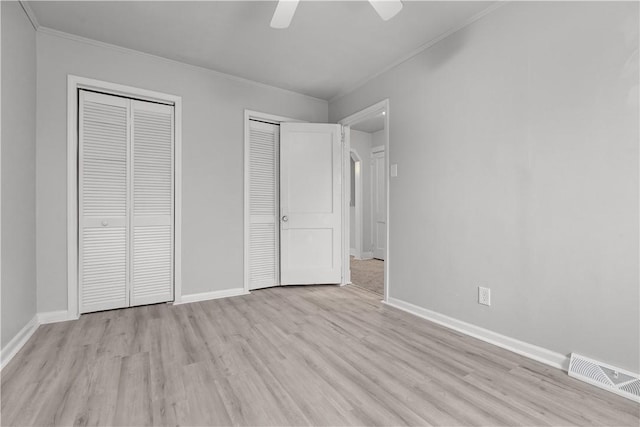 unfurnished bedroom featuring light wood-type flooring, two closets, ceiling fan, and crown molding