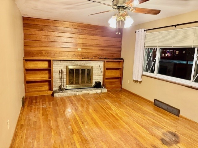 unfurnished living room featuring a stone fireplace, ceiling fan, wood walls, and hardwood / wood-style flooring