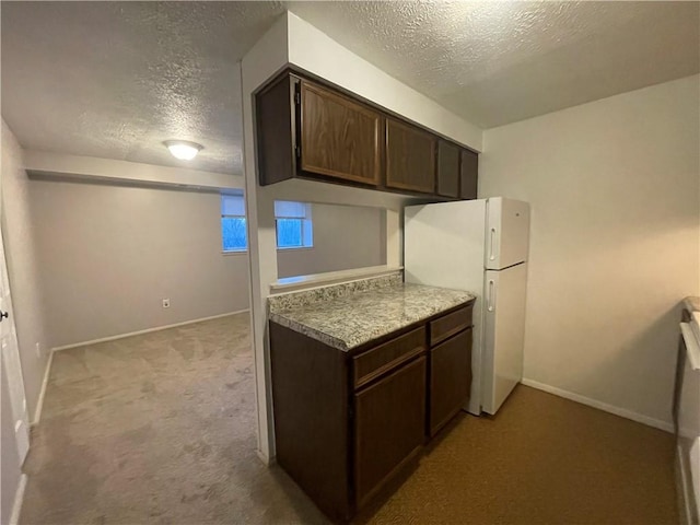 kitchen featuring a textured ceiling, dark brown cabinetry, light colored carpet, and white fridge