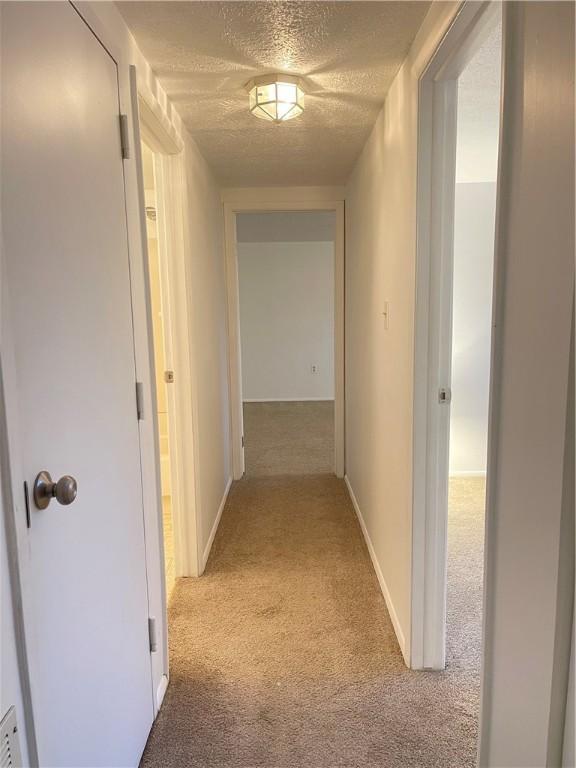 corridor featuring light carpet and a textured ceiling