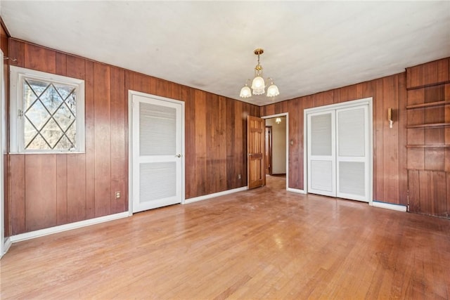 unfurnished room featuring light hardwood / wood-style flooring, a notable chandelier, and wood walls