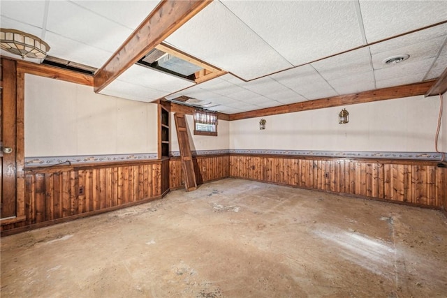 basement featuring a drop ceiling and wood walls