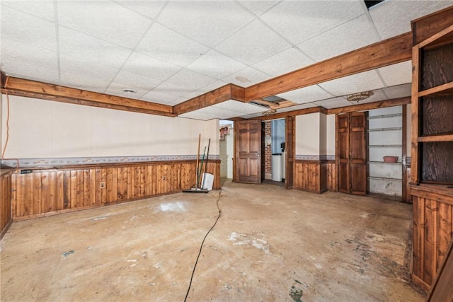 misc room with concrete flooring, a drop ceiling, and wooden walls