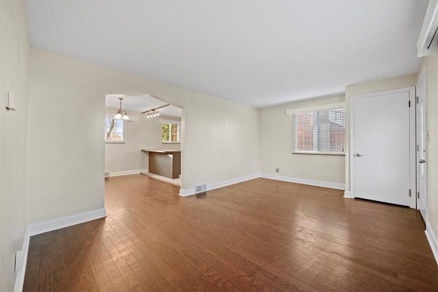 unfurnished living room featuring dark hardwood / wood-style flooring, an inviting chandelier, and a wealth of natural light