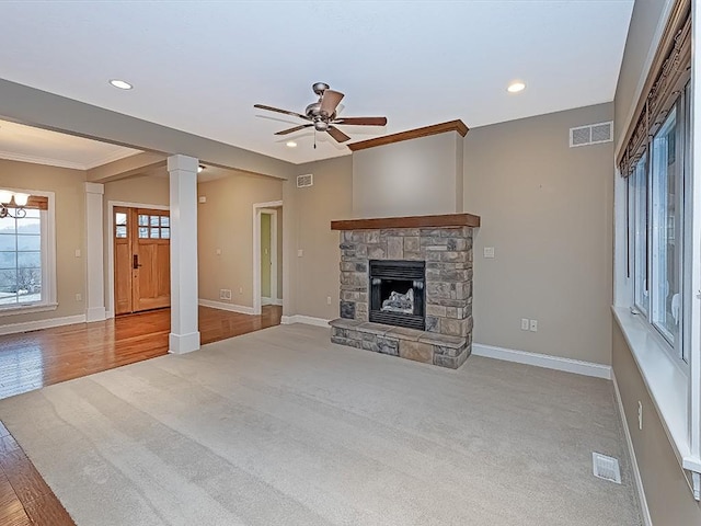 unfurnished living room featuring a stone fireplace, light hardwood / wood-style floors, ceiling fan with notable chandelier, and ornamental molding