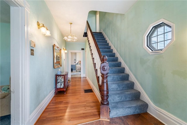 stairway with hardwood / wood-style flooring and a notable chandelier