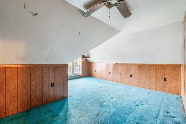 bonus room with wood walls, ceiling fan, vaulted ceiling, and dark colored carpet