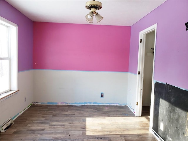 empty room featuring hardwood / wood-style flooring, a healthy amount of sunlight, and a baseboard radiator