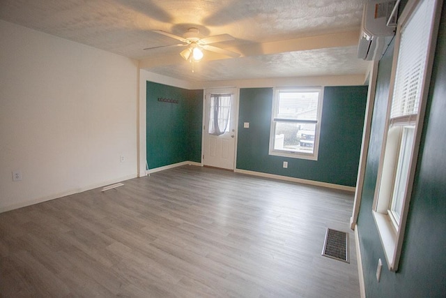 empty room featuring a wall mounted air conditioner, a textured ceiling, light hardwood / wood-style floors, and ceiling fan