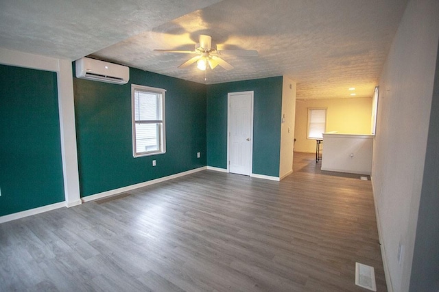 unfurnished room with a textured ceiling, ceiling fan, dark hardwood / wood-style flooring, and a wall mounted air conditioner