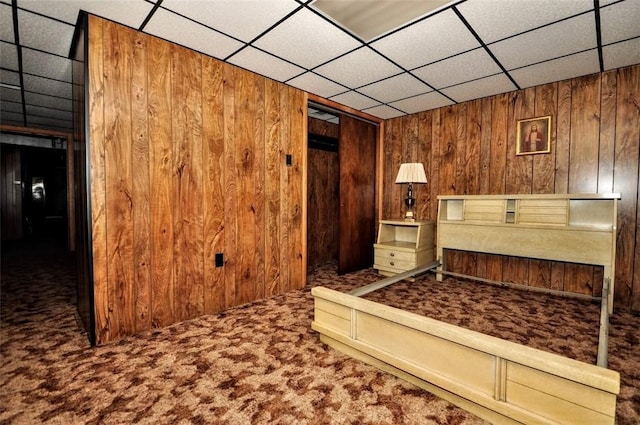 carpeted bedroom with a paneled ceiling, a closet, and wooden walls