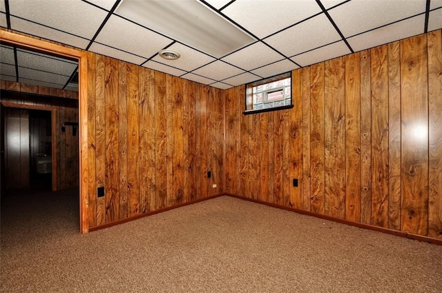 basement with a drop ceiling, carpet floors, and wooden walls