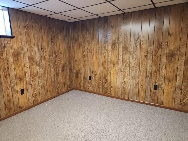 basement featuring carpet, a drop ceiling, and wood walls