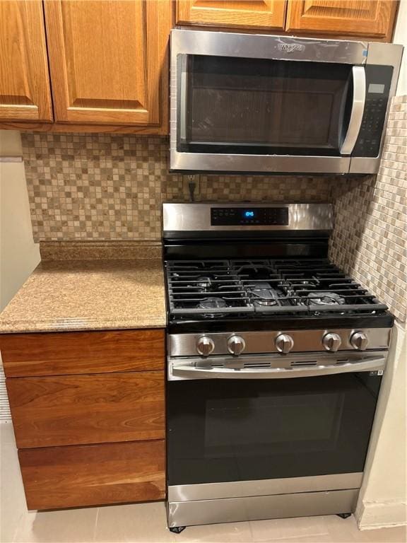 kitchen with light stone counters, backsplash, and appliances with stainless steel finishes