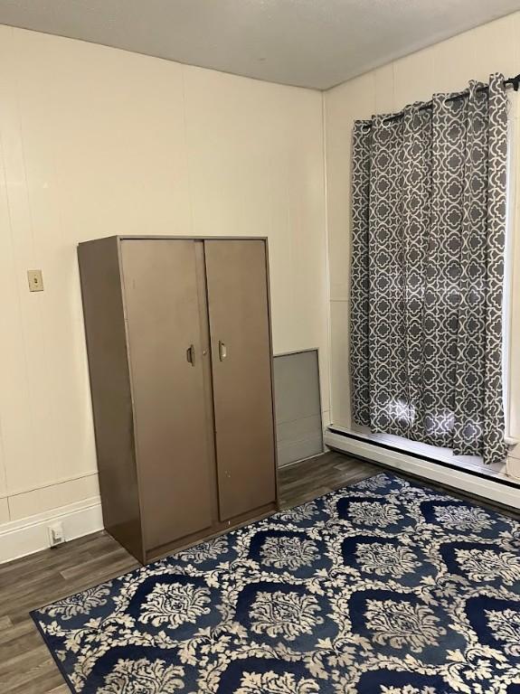 bedroom with a closet, dark hardwood / wood-style flooring, and a baseboard heating unit