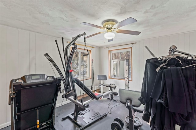 exercise room with a textured ceiling, ceiling fan, and wooden walls