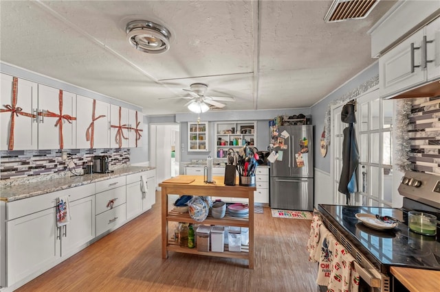 kitchen featuring light wood-type flooring, stainless steel appliances, white cabinetry, and light stone counters