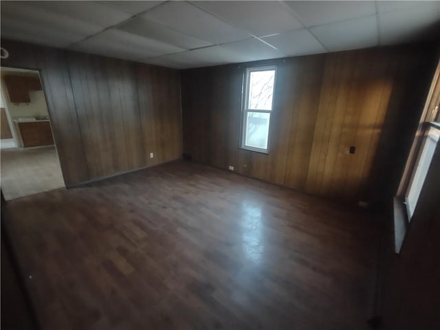 spare room featuring a drop ceiling, dark wood-type flooring, and wood walls