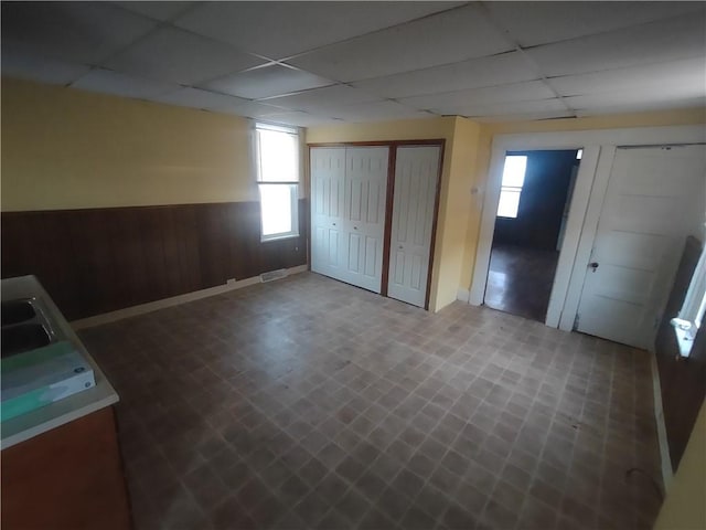 unfurnished bedroom with a closet, wood walls, a drop ceiling, and sink