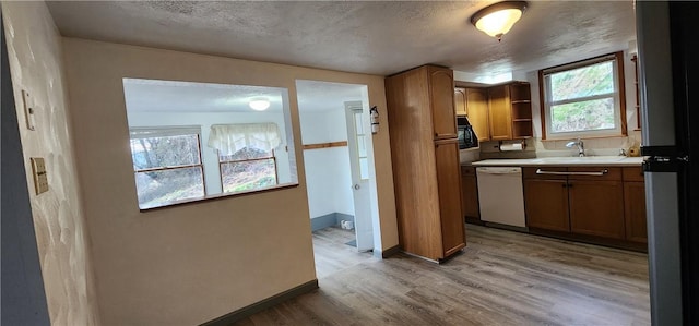 kitchen with dishwasher, a textured ceiling, light hardwood / wood-style flooring, and sink