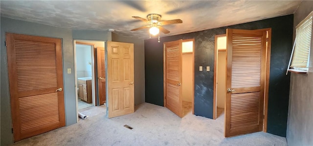 unfurnished bedroom with ceiling fan, light carpet, and multiple closets