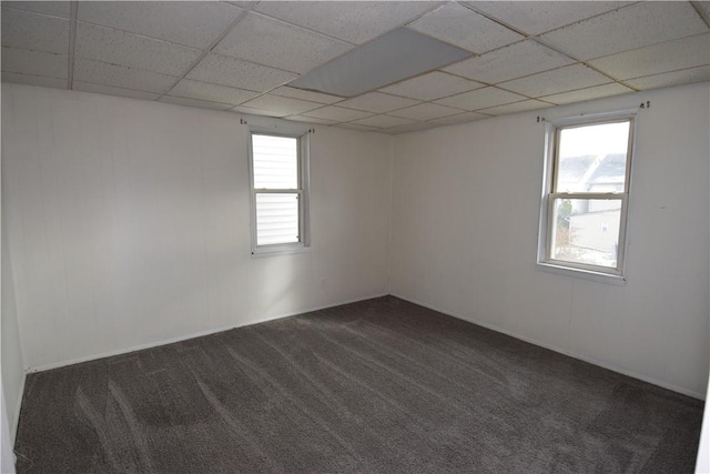 empty room with a drop ceiling, a healthy amount of sunlight, and dark colored carpet