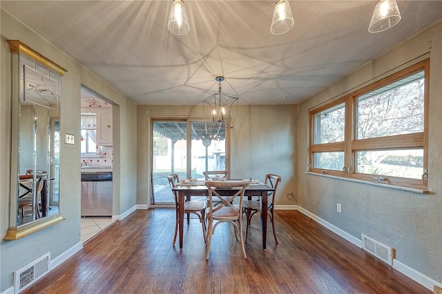 dining space with a healthy amount of sunlight, wood-type flooring, and an inviting chandelier