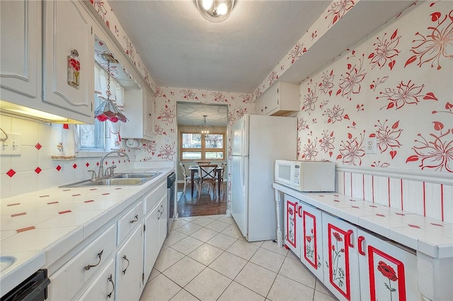 kitchen featuring tile countertops, white appliances, sink, light tile patterned floors, and white cabinetry