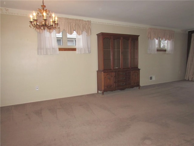 carpeted spare room featuring plenty of natural light and an inviting chandelier