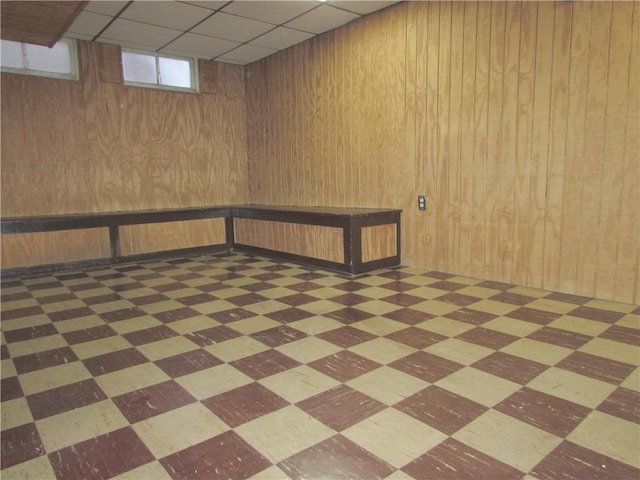 basement featuring wood walls and a drop ceiling