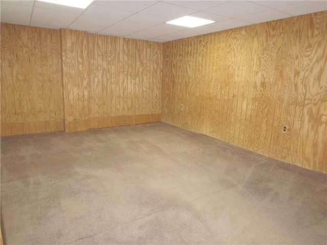 basement featuring a paneled ceiling and wood walls