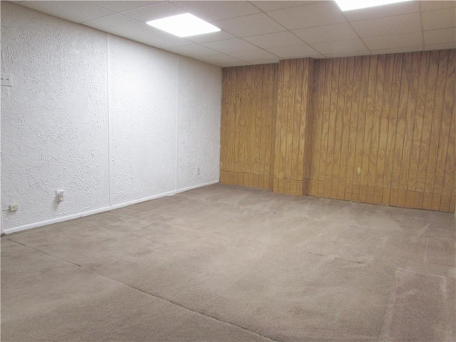 unfurnished room featuring wooden walls, a drop ceiling, and carpet floors