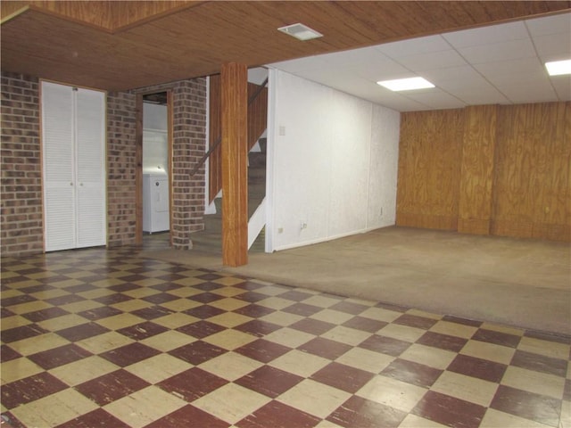 basement with brick wall, dark carpet, and wood walls