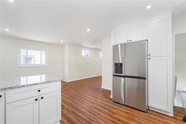 kitchen with stainless steel fridge, white cabinets, light stone counters, and light wood-type flooring