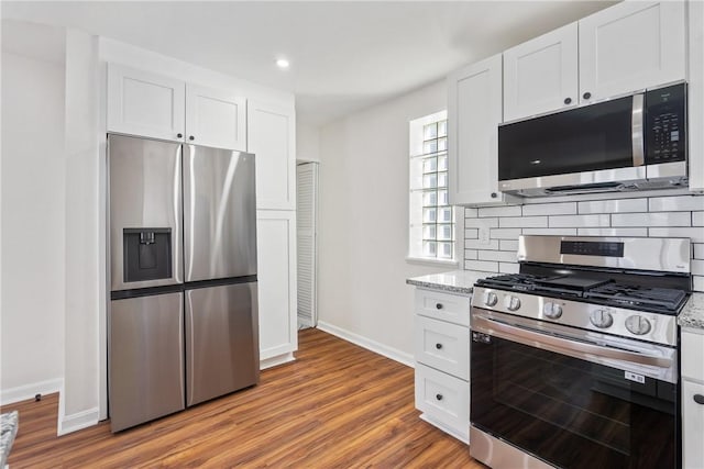 kitchen featuring light stone countertops, stainless steel appliances, backsplash, white cabinets, and light wood-type flooring