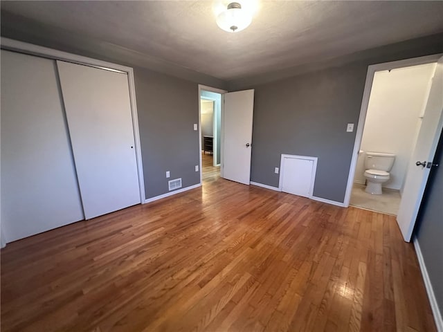 unfurnished bedroom with hardwood / wood-style floors, ensuite bathroom, and a closet